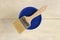 A paint brush is lying on the blue lid of a plastic paint bucket on an old white vintage wooden plank table. Place for text or