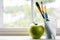 Paint brushes with a green apple next to window