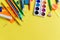 Paint, pencils and scissors. School accessories on a yellow background. View from above