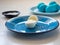 Painted eggs lie on two blue ceramic plates. Blue eggs are unpeeled and a single egg is cut in half