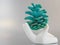 A painted green cone of a New Year tree lies on a porcelain hand against a gray background