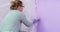 The painter girl paints the wall with a roller and a brush in lilac color. Professional repair and painting of walls