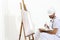 Painter man with canvas on easel, palette and brush, isolated on