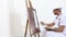Painter man at work with paint roller, easel, canvas and palette, wall painting concept, white background