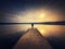 Painting of a man standing alone on the pier facing the sunset reflected on the calm lake water. Scenic view with a lonely person