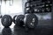 A pair of 5 kilogram dumbbells lying on the floor of a gym, with a dumbbell rack visible in the background.