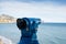 Pair of binoculars lay on the sand of a beach, with the vast blue ocean in the background