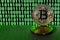 A pair of bitcoins lies on a cardboard surface on the background of a monitor depicting a binary code of bright green zeros and on