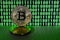 A pair of bitcoins lies on a cardboard surface on the background of a monitor depicting a binary code of bright green zeros and on