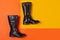 A pair of black leather boots lies on an orange and yellow background, the concept of fashion