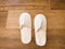 Pair of blank soft white home slippers on the wooden floor.