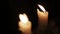 Pair of burning candles in a dark room. Two wax candles in close-up view burn in a dark room amid sharply blinking glare