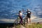 Pair cyclists on top of mountain give each other high five against cloudy sky at sunset