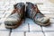 A pair of dirty boots. Old worn dark blue leather shoes with variegated brown laces. Background from gray pavers. The concept of