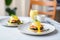 a pair of eggs benedicts on a plate with a small bowl of hollandaise