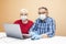 A pair of elderly people in medical masks and gloves are sitting at a table with a laptop