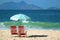 Pair of empty red beach chairs with light blue parasol on the sandy beach against the crashing waves of Atlantic ocean