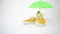 A pair of fashionable mustard-colored shoes. A hand puts a green umbrella over a shoe. Sun protection