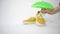 A pair of fashionable mustard-colored shoes. A hand puts a green umbrella over a shoe. Sun protection