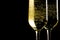 A pair of flutes of champagne with golden bubbles on black background