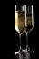 A pair of flutes of champagne with golden bubbles on black wood background