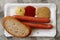 Pair of frankfurter sausages with a slice of bread on paper plat