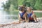 Pair of French Bulldogs with matching maritime sailor collar dog harnesses sitting at pebble beach of lake