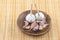Pair of garlic heads and a scattering of cloves folded in a wooden plate stands on a light beige background