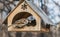 A pair of gray and brown sparrows eats in an old yellow bird and squirrel feeder house from plywood in the park