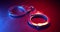 Pair of handcuffs used by law enforcement to arrest criminals, lit in red and blue police lights. Justice or catching a guilty