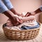 A pair of hands folding freshly laundered clothes, with a laundry basket full of clothes