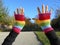 pair of hands wearing a rainbow colored hand made crochet fingerless gloves