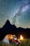 Pair hikers sitting near glowing tent and campfire, looking to the shines starry sky in the camping at night