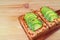 Pair of homemade grilled cheese toast topped with tomato and sliced avocado on wooden table