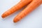 Pair long fresh raw carrot on a plastic cutting board is white color.