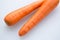 Pair long fresh raw carrot on a plastic cutting board is white color.