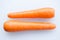 Pair long fresh raw carrot on a plastic cutting board is white color.