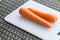 Pair long fresh raw carrot on a plastic cutting board is white color.