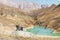 A pair of old leather vintage shoes stand on a stone against the backdrop of a mountain turquoise lake and epic rock