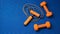 Pair of orange dumbbells and jumping rope on blue yoga mat background