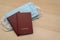 A pair of passports lie on a pack of medical masks on a wooden table.