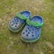 a pair of plastic sandals.  for babies.  blue.  with a green background