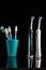 Pair of Professional Electric Toothbrushes In Front of Four Manual Toothbrushes Placed on One Cup Together On Black