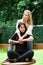 A pair of proud lesbian in outdoors sitting on a wooden table, blonde woman is hugging a brunette woman, in a garden