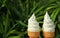 Pair of pure white milk soft serve ice cream cones in the sunlight, with blurred green foliage