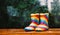 Pair of rainbow rain boots sitting outside with a rainy blurred out background