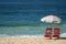 Pair of red beach chairs and pale pink parasol on the sandy beach against ocean waves