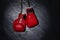 Pair of red boxing gloves hanging in spotlight on grey stone background. Space for text