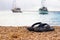 A pair of rubber footwear in the beach on the sand.