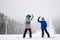Pair of snowboarders giving high five standing on ski run with chairlift. Dense foggy views in snowfall on background